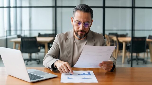 Businessman analyzing financial documents at office desk with laptop
