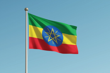 Naklejka premium Ethiopia national flag waving on pole against clear blue sky background.