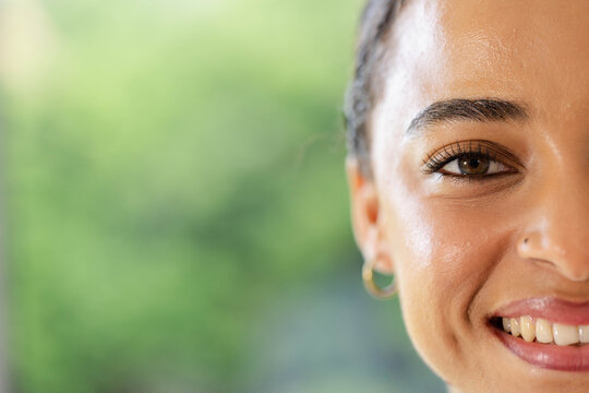 African American woman smiling, showing gold hoop earring and nose stud in garden, copy space