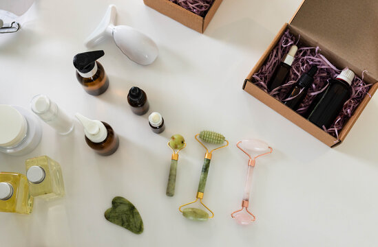 Three facial rollers and gua sha stone resting on white tabletop with skincare bottles nearby
