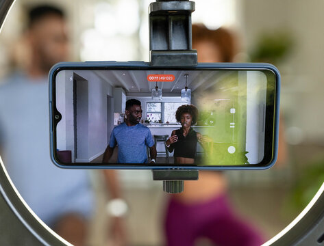 Couple filming in kitchen on ring-light showing red timer, man blue tee woman black crop top