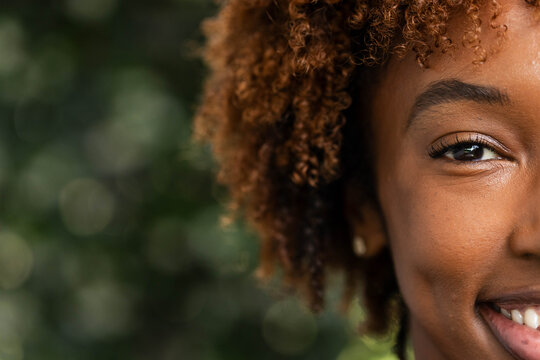 Right face half is smiling in soft daylight with curly brown ringlets and gold stud earring