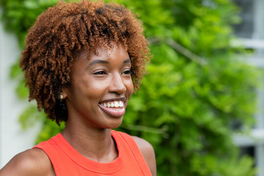 African American adult woman smiling and looking right in garden, wearing red top, stud earrings