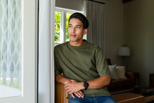 Man sitting on arm of brown leather sofa in living room, wearing olive-green T-shirt and wristwatch