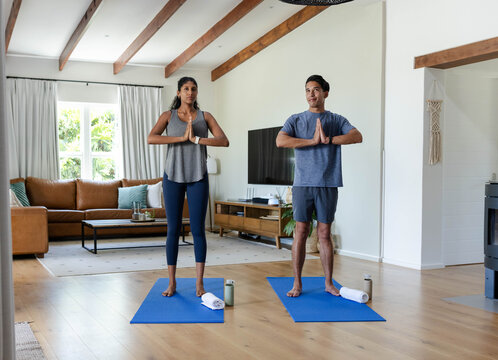 African American couple practicing yoga on blue mats in living room, holding prayer pose