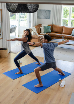 Two people are practicing yoga on blue mats in home living room by sliding glass door
