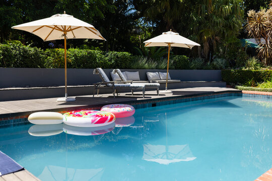 Turquoise pool holding three inflatable rings near wooden deck, umbrellas showing reflections
