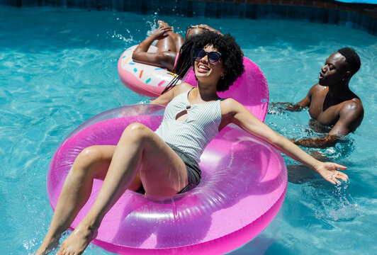 Transparent pink donut float is floating in clear pool water with pastel sprinkle float nearby