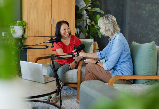 Diverse female cohosts, senior and Asian women, recording podcast at home with microphones, laptop