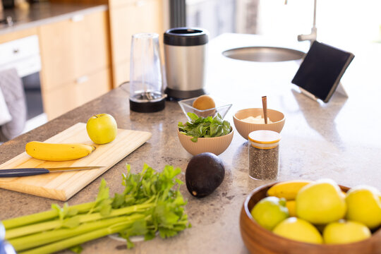 Wooden cutting board holding banana and green apple, knife resting on stone countertop near blender