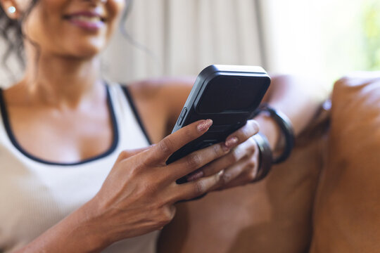 Smartphone being held with thumbs typing on brown leather sofa near window, blurred greenery