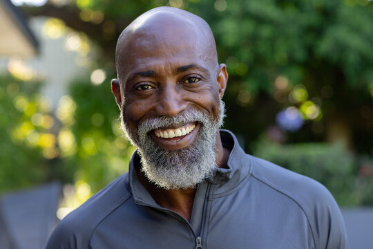 Senior African American man smiling and facing camera, wearing gray zip-up pullover in garden