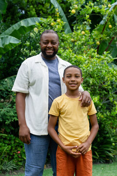 African American father and son smiling in garden in casual clothes, showing citrus tree