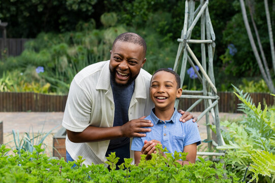 African American father and boy laughing among garden plants with trellis in backyard patio