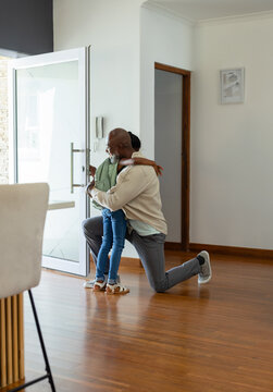 Grandfather is kneeling and hugging granddaughter near open glass door on hardwood floor
