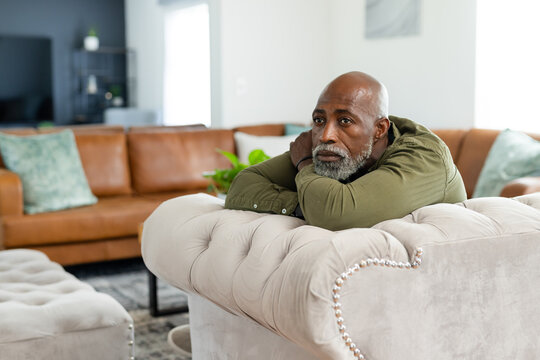 Senior African American man leaning on tufted beige sofa at home, wearing olive shirt, copy space