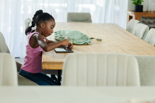 Tablet receiving stylus input while resting on long wooden dining table near green backpack