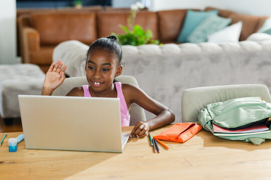 Silver laptop and colorful school supplies are sitting on wooden table near sofa, home study