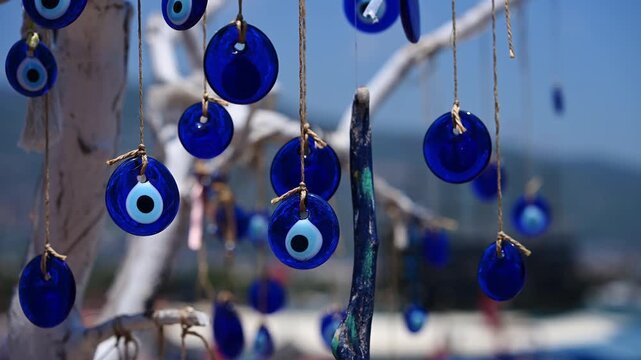 Colorful nautical-themed jewelry. Nazar amulet pendants sway against port landscapes. Elegant Blue Eye amulets hang delicately from sunlit white branch. Amulets against evil eye in Turkic countries