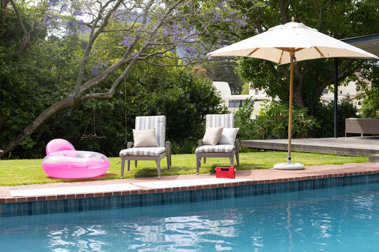 Blue tiled pool reflecting sunlight and casting shadows on brick coping, chairs near pink ring