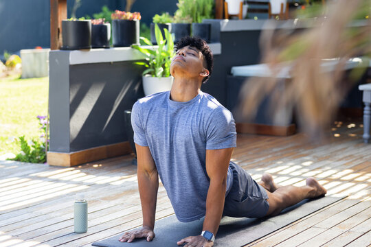 African American man practicing yoga backbend on mat on deck in athletic shirt with water bottle