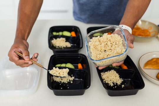 Hands are portioning cooked quinoa into three black divided meal trays on countertop