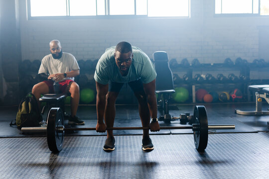 African American men gripping loaded barbell at gym, lifter wearing light shirt, dark shorts