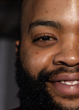 Right half of male face is showing in dark room, with beard, mole, soft directional light