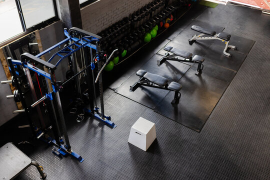 White plyometric box is sitting on black rubber floor near blue cable machine and benches