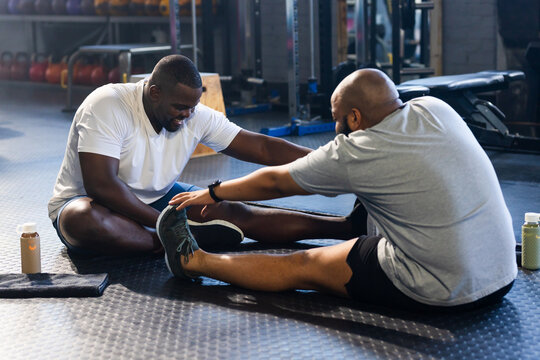 African American men stretching and reaching on gym floor, wearing tees and shorts with kettlebells