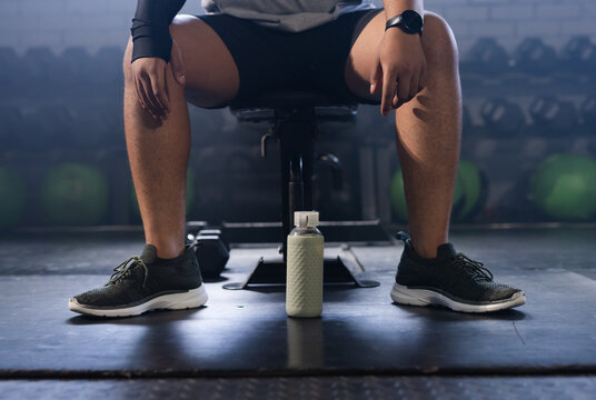 Textured flip-top water bottle resting on rubber gym mat before weight bench, dumbbells nearby
