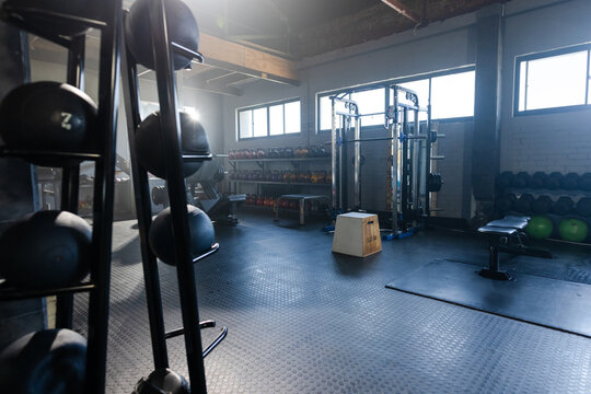 Vertical medicine ball rack is holding black balls on rubber floor in gym, near plyometric box