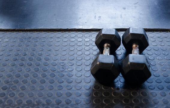 Pair of hexagonal rubber-coated dumbbells resting on right-side rubber gym mat, showing scuff marks