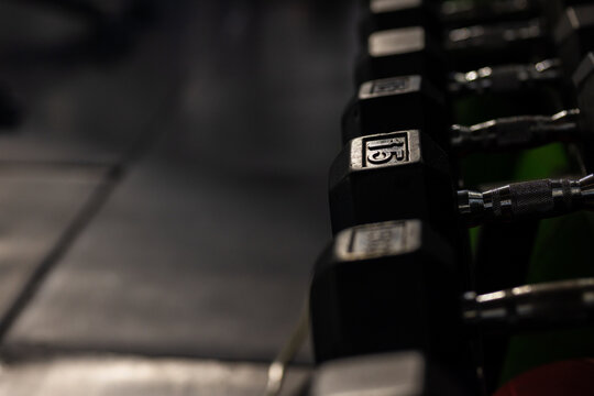 Single black hex dumbbell resting on rack in gym, showing chrome handle and floor reflections