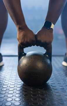 Kettlebell being gripped by hands on textured rubber gym floor, 12KG stamping visible