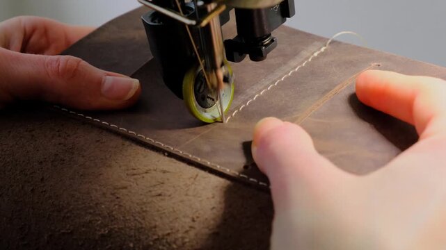 Close-up shot of an industrial sewing machine stitching thick leather during production of a handmade leather journal. Traditional craftsmanship and precision sewing in a small leather workshop.