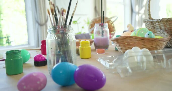Camera is panning right across craft table, revealing painted eggs and brushes for Easter