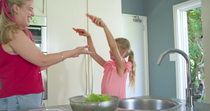 Mother and daughter prepping meal at sink after child scrubbing carrot, rinsing lettuce in colander