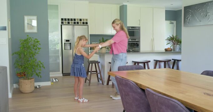 Mother and daughter placing plant on kitchen island, holding hands, spinning and laughing for play
