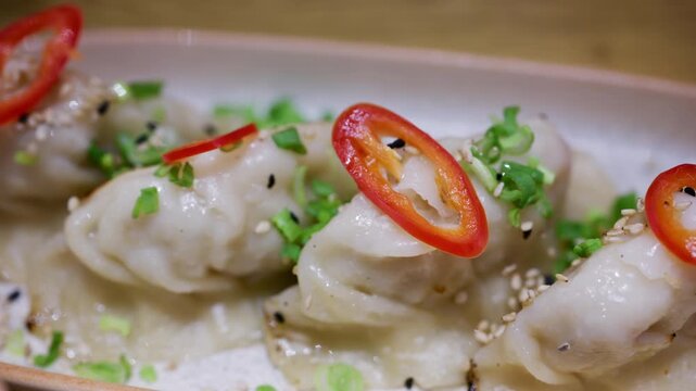 Row of pan fried dumplings topped with sliced red chili and green onions on a ceramic plate