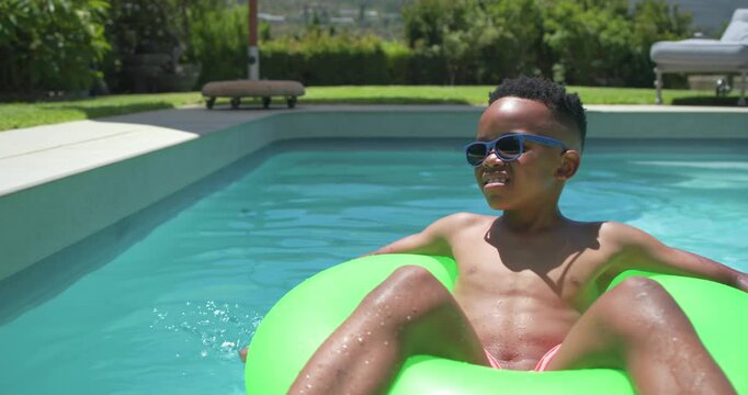 Preteen boy shifting weight, splashing to steer green ring at pool drifting wearing shades to relax