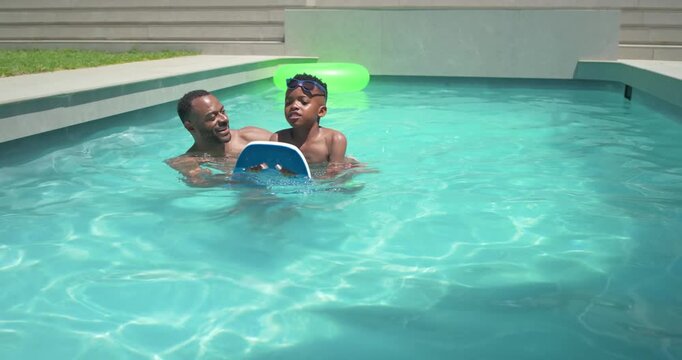 African American father and child learning in home pool as dad easing hold, gripping blue kickboard