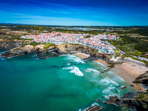 Aerial view of the village nestled atop rugged cliffs, where the whitewashed houses meet the turquoise sea in Zambujeira do Mar, Beja District, Portugal.