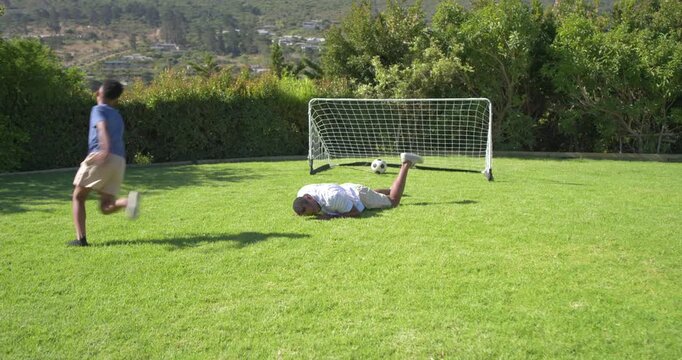 African American father and teen son placing ball dribbling shooting past father diving at goal
