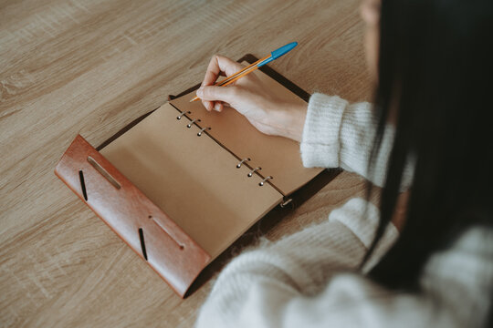 Une femme &eacute;crivant &agrave; la main dans un carnet artisanal sur une table en bois