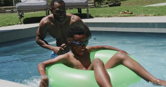 African American father and son, father entering pool bracing green ring and pushing son for safety