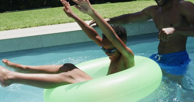 African American father and son nudging neon ring at pool, boy kicking, father steadying for fun
