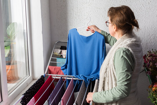 A woman around 50 years old is hanging clothes on a drying rack outside her balcony. She carefully organizes items to let them dry in the sunlight during the afternoon