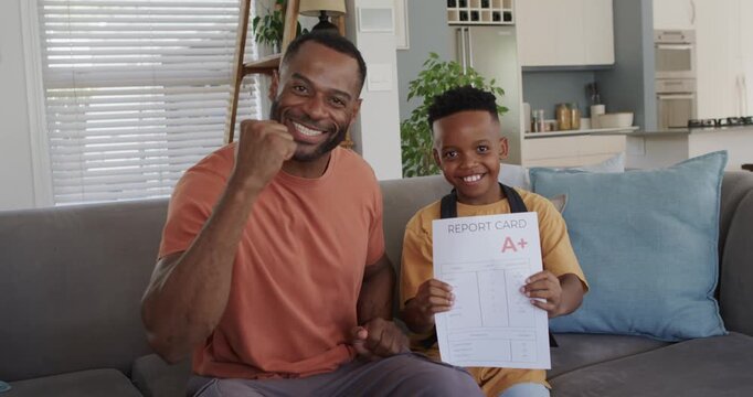 African American father and son celebrating, son holding report card showing uppercase A+ on couch