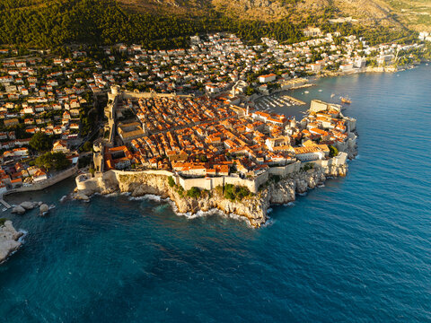 Aerial view of the ancient city walls embracing the terracotta rooftops as the turquoise Adriatic Sea crashes against the rocky shores, Dubrovnik, Dubrovnik-Neretva County, Croatia.